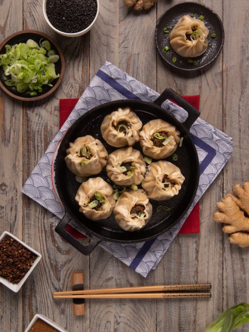 Baozi con manzo e cipolle in padella di ferro, guarniti con cipollotto fresco e sesamo nero