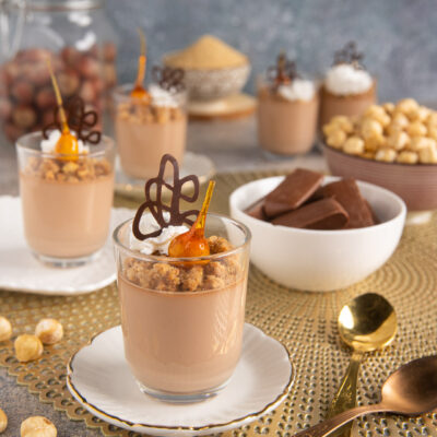 Cremoso ai gianduiotti servito in bicchiere con crumble alle nocciole, decorazione di cioccolato e caramello
