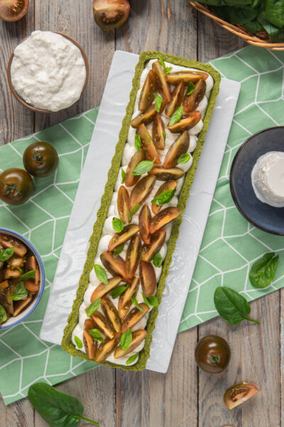 Crostata salata con base verde agli spinaci, stracciatella e fette di pomodoro kumato con basilico
