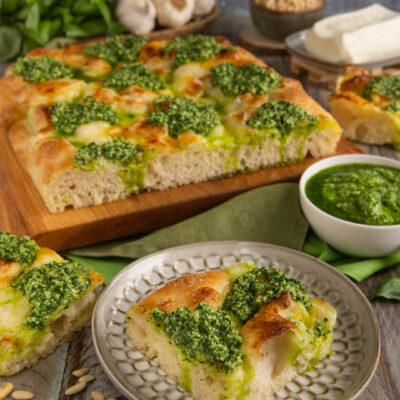 Focaccia al pesto e stracchino tagliata a quadrotti con ciuffi di pesto e crosta dorata
