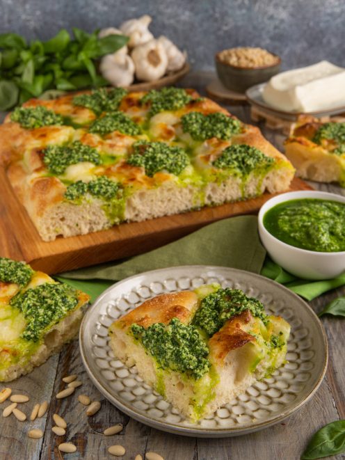 Focaccia al pesto e stracchino tagliata a quadrotti con ciuffi di pesto e crosta dorata