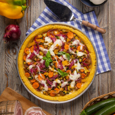 Pizza di polenta con verdure grigliate, mozzarella filante e basilico fresco, servita in teglia