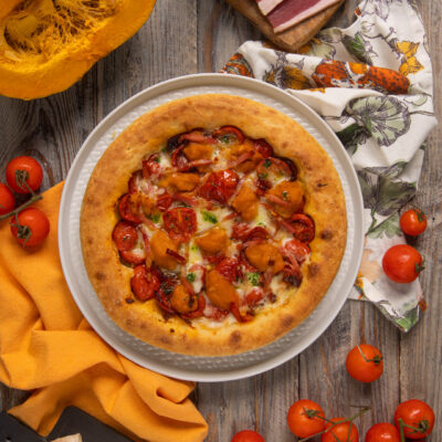Pizza gourmet con crosta alta, cubetti di zucca, pomodorini confit e speck croccante
