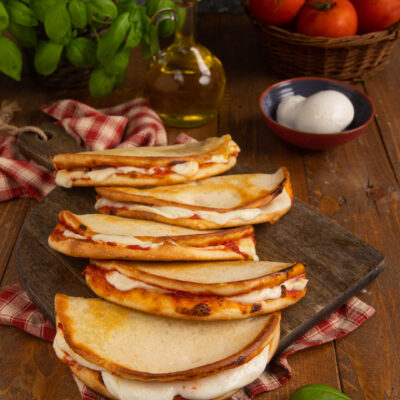 Pizzette da passeggio piegate a mezzaluna con mozzarella filante e pomodoro, disposte in fila su tagliere