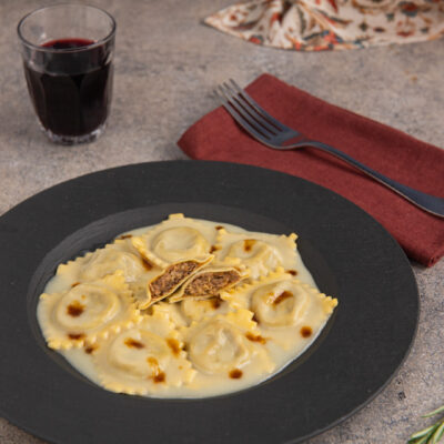 Ravioli di brasato conditi con vellutata di patate e gocce di fondo bruno, uno aperto a mostrare il ripieno