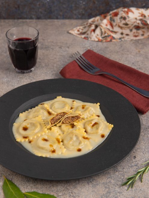 Ravioli di brasato conditi con vellutata di patate e gocce di fondo bruno, uno aperto a mostrare il ripieno