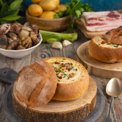 Zuppa di vongole nella pagnotta di pane sfornata, servita con prezzemolo e guanciale croccante