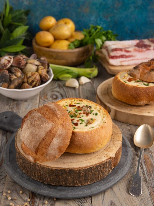 Zuppa di vongole nella pagnotta di pane sfornata, servita con prezzemolo e guanciale croccante
