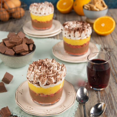 Zuppa inglese di biscotti servita in bicchierini con strati di cioccolato, crema gialla e panna al cacao