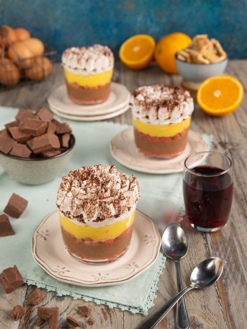 Zuppa inglese di biscotti servita in bicchierini con strati di cioccolato, crema gialla e panna al cacao