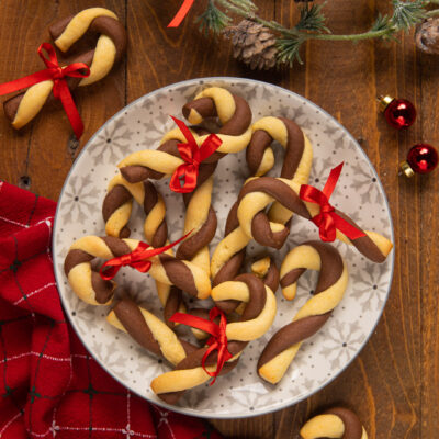 Biscotti di Natale Candy Cane bicolore a forma di bastoncino con fiocchetti rossi su piatto decorato
