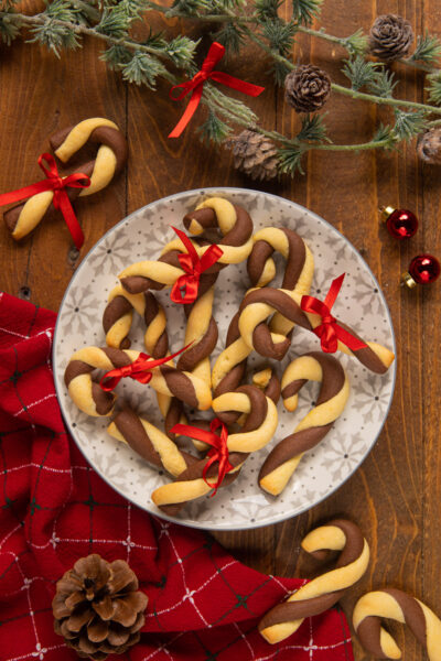Biscotti di Natale Candy Cane bicolore a forma di bastoncino con fiocchetti rossi su piatto decorato