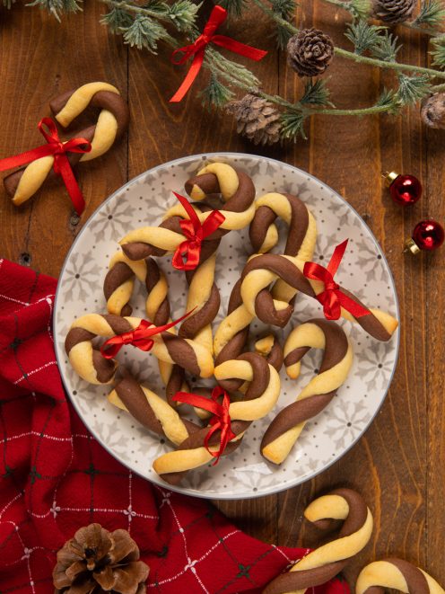Biscotti di Natale Candy Cane bicolore a forma di bastoncino con fiocchetti rossi su piatto decorato