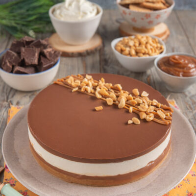 Cheesecake al caramello con strato di mousse bianca, glassa al cioccolato e arachidi tostate in superficie