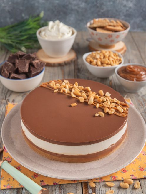 Cheesecake al caramello con strato di mousse bianca, glassa al cioccolato e arachidi tostate in superficie