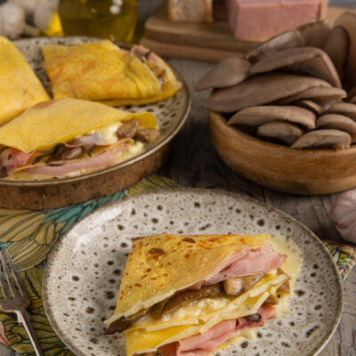 Crepes ripiegate con funghi, taleggio filante e prosciutto affumicato servite su piatto rustico