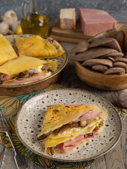 Crepes ripiegate con funghi, taleggio filante e prosciutto affumicato servite su piatto rustico