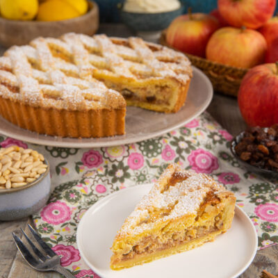Crostata di mele con mascarpone, uvetta e pinoli, una fetta servita con il ripieno dorato in vista e zucchero a velo
