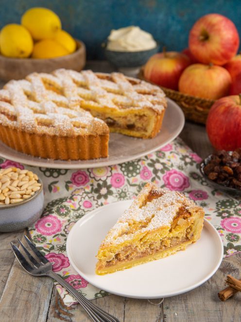 Crostata di mele con mascarpone, uvetta e pinoli, una fetta servita con il ripieno dorato in vista e zucchero a velo