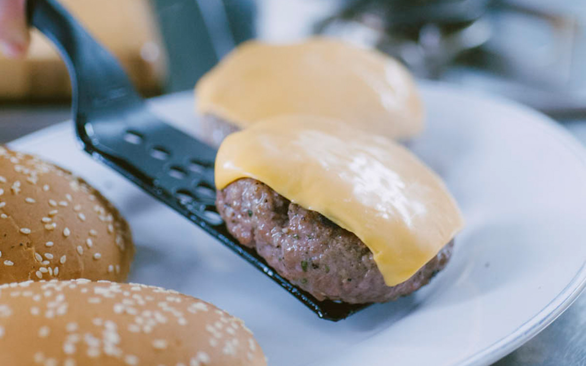 Hamburger con fetta di cheddar fuso sollevato con una spatola, pronto per essere adagiato sul panino