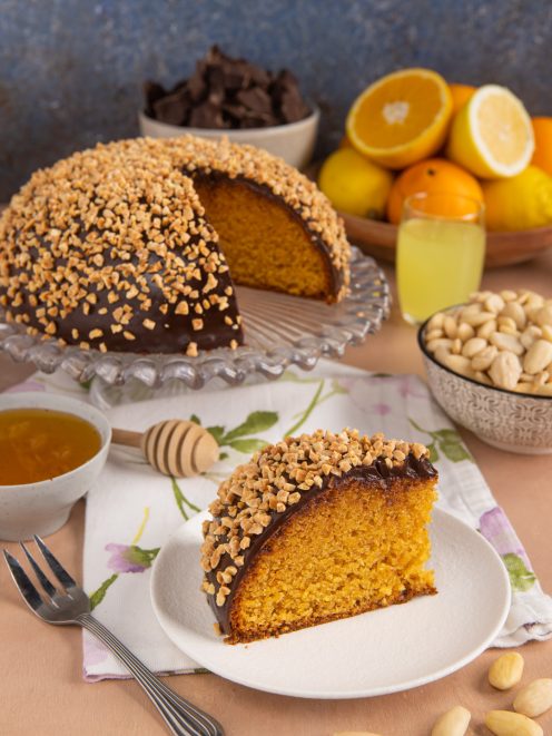 Mandorlaccio a cupola con glassa al cioccolato e granella di mandorle, servito a fette con cuore soffice all'arancia