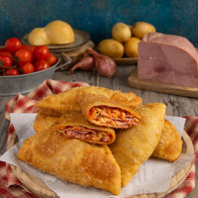 Panzerotti di patate fritti e croccanti tagliati a metà con ripieno filante di pomodoro e prosciutto