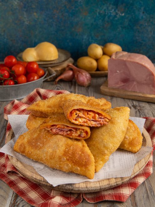Panzerotti di patate fritti e croccanti tagliati a metà con ripieno filante di pomodoro e prosciutto
