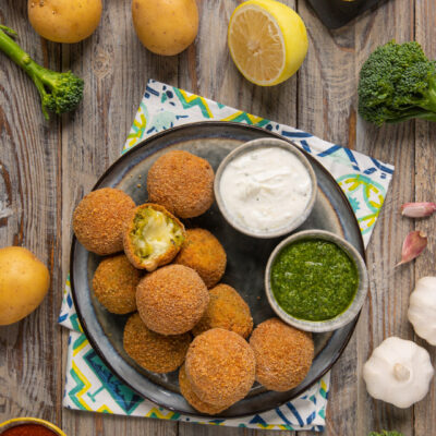 Polpette di broccoletti con cuore filante impanate e fritte, servite con salsa allo yogurt e pesto