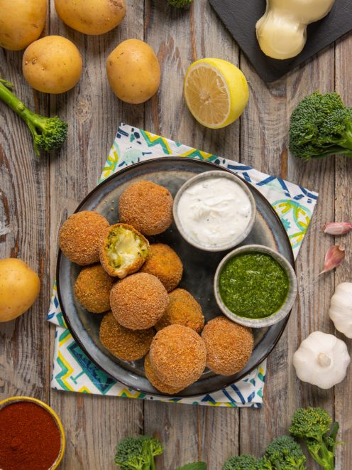 Polpette di broccoletti con cuore filante impanate e fritte, servite con salsa allo yogurt e pesto