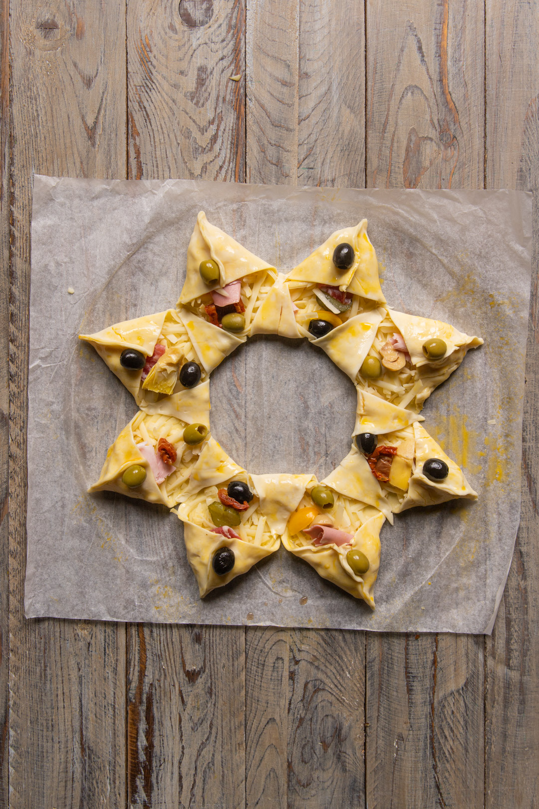 Stella di sfoglia farcita con prosciutto e formaggio, olive intere sui triangoli esterni prima della cottura