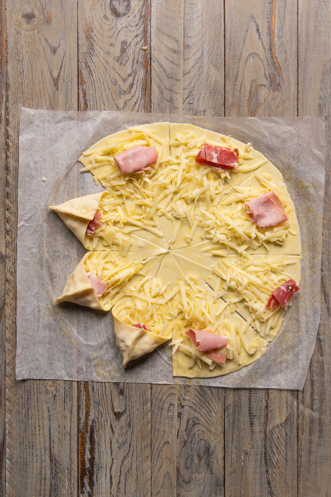 Spicchi di pasta sfoglia farciti con formaggio grattugiato e salume ripiegati a punta a formare una stella