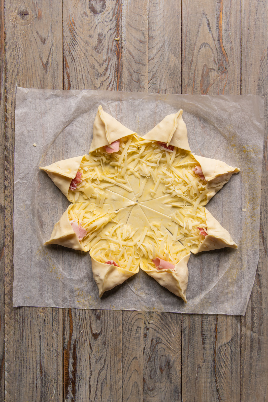 Punte di pasta sfoglia ripiegate a stella su prosciutto e formaggio grattugiato prima della cottura