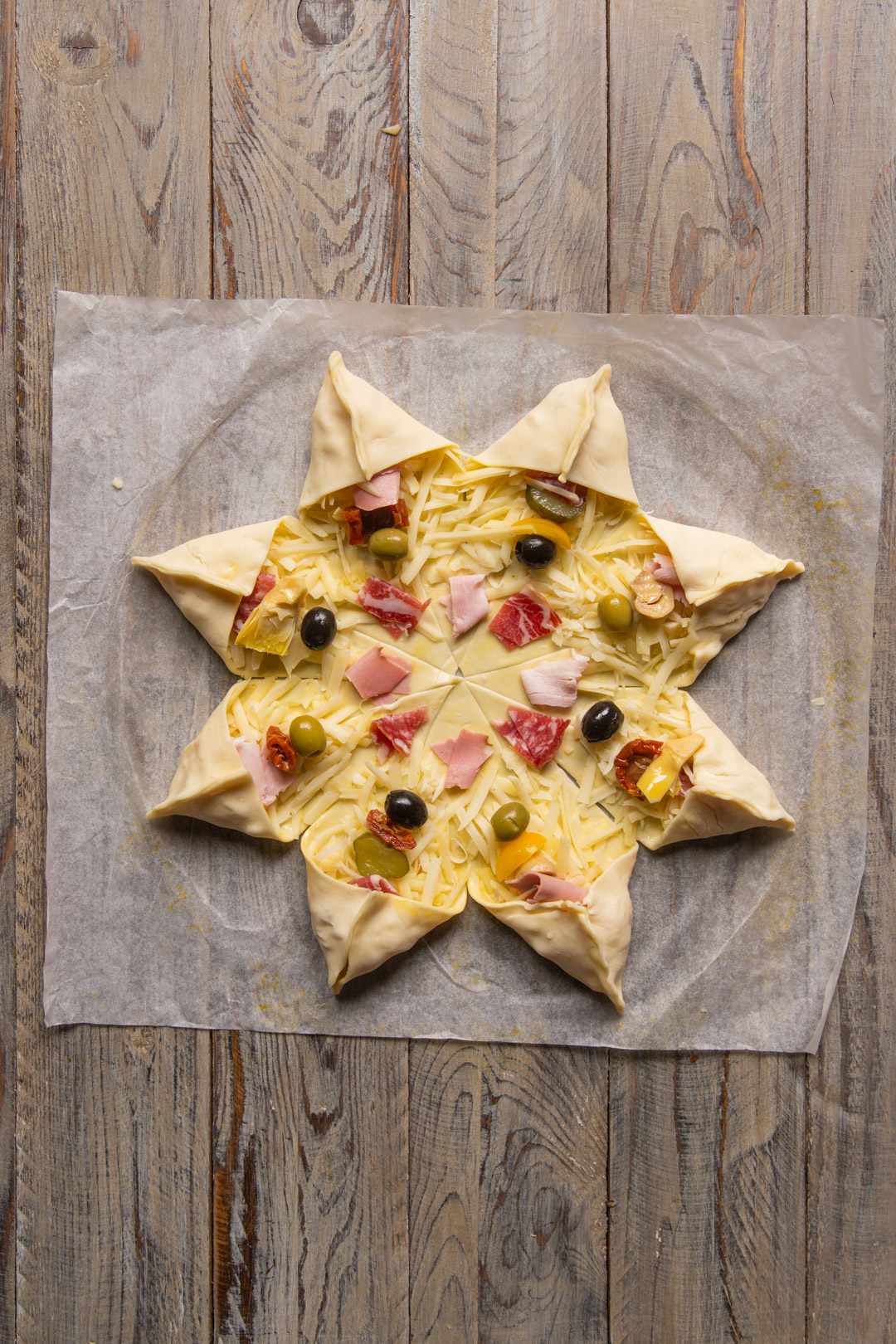 Stella di sfoglia farcita con formaggio, salumi e olive prima di ripiegare le punte
