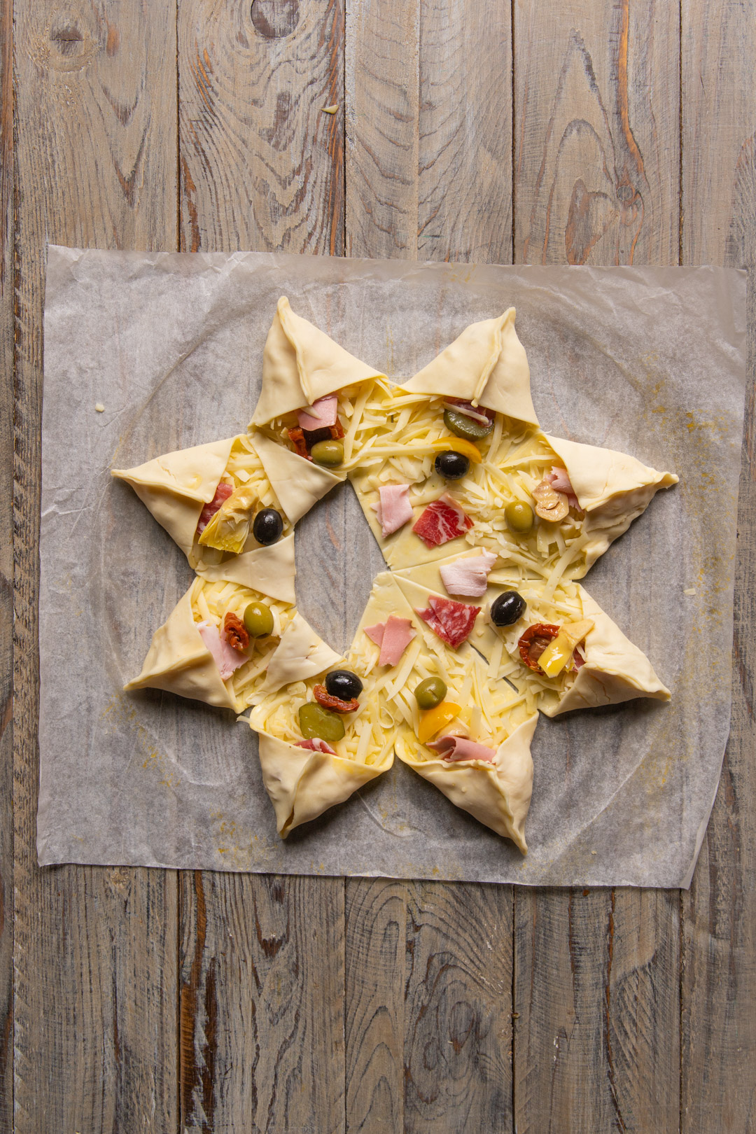 Punte di pasta sfoglia ripiegate a stella con formaggio, salumi e olive prima della cottura