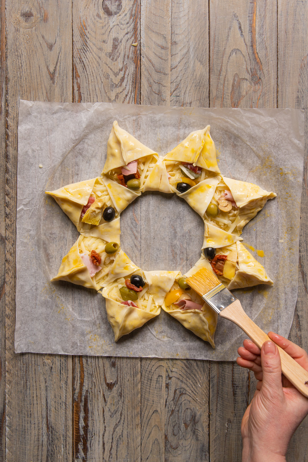Pennello spennella con uovo la stella di sfoglia farcita con prosciutto, olive e formaggio