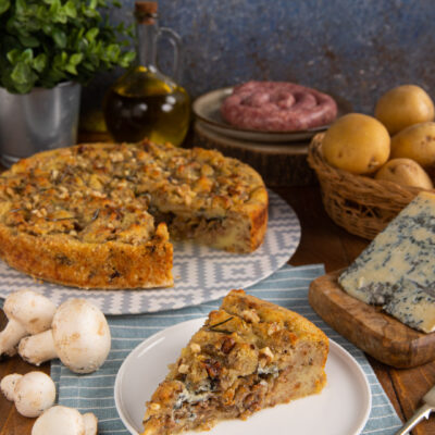 Sbriciolata di patate con salsiccia e funghi tagliata a fette, guarnita con noci e rosmarino