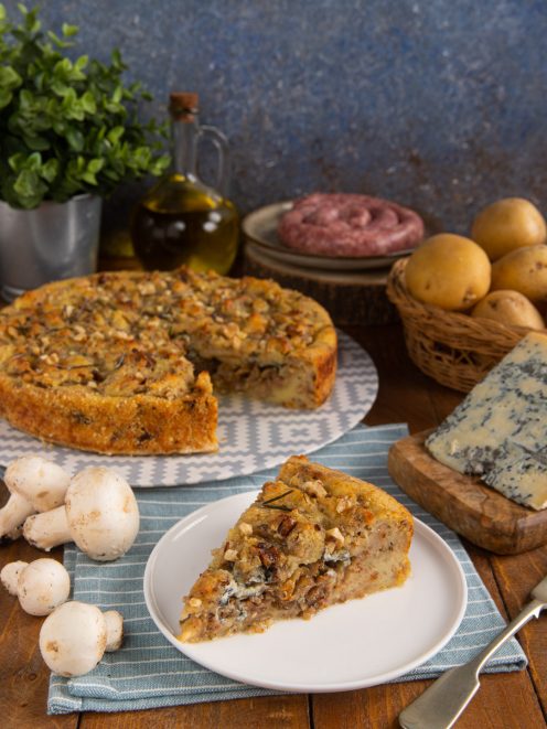 Sbriciolata di patate con salsiccia e funghi tagliata a fette, guarnita con noci e rosmarino