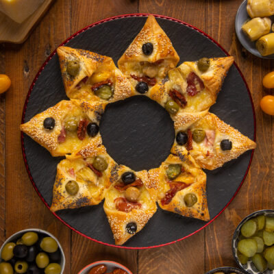 Stella di sfoglia salata farcita con olive, pomodori secchi e formaggio filante, servita con antipasti misti