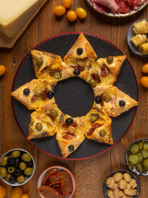 Stella di sfoglia salata farcita con olive, pomodori secchi e formaggio filante, servita con antipasti misti
