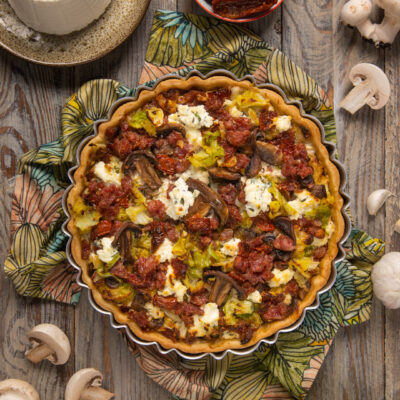 Torta salata con verze, funghi, ricotta e pomodori secchi appena sfornata su canovaccio fiorato