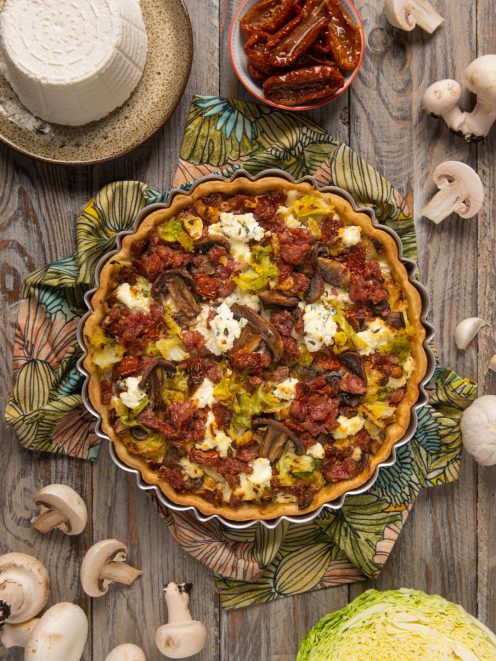 Torta salata con verze, funghi, ricotta e pomodori secchi appena sfornata su canovaccio fiorato