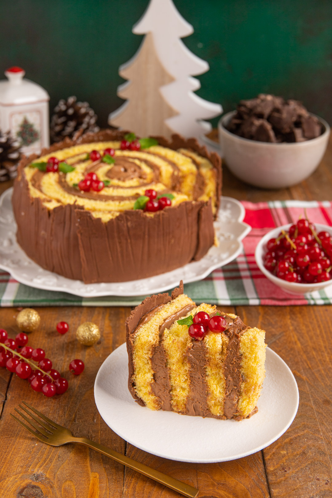 Torta tronco di Natale a spirale con fetta a strati decorata da ribes rossi e foglioline di menta