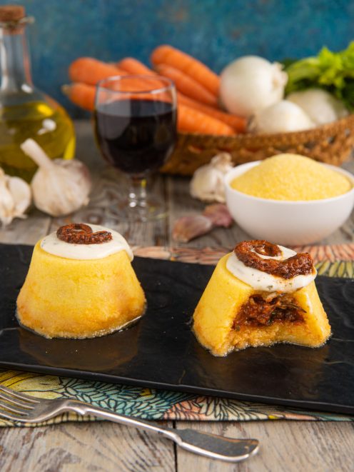 Tortini di polenta ripieni di ragù di polpo, aperti a mostrare il cuore e nappati con crema alle erbe