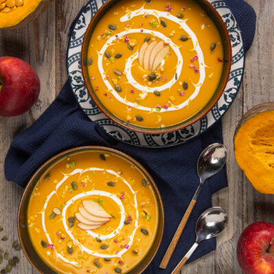 Vellutata di mele e zucca guarnita con panna, semi di zucca e fettine di mela in due ciotole