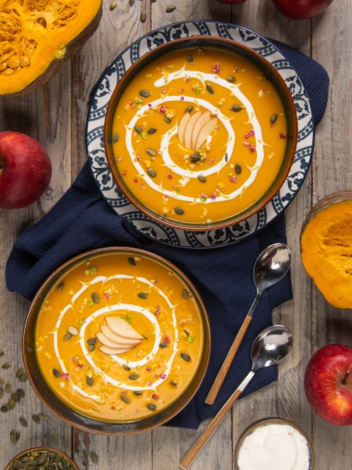 Vellutata di mele e zucca guarnita con panna, semi di zucca e fettine di mela in due ciotole