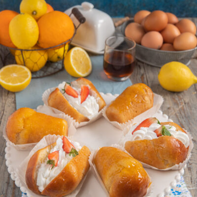 Babà al rum farciti con panna montata e fragole fresche, serviti nei pirottini