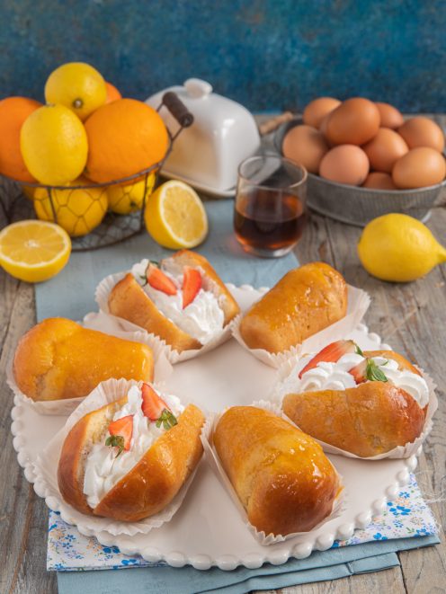 Babà al rum farciti con panna montata e fragole fresche, serviti nei pirottini