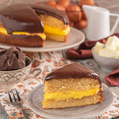 Fetta di Boston cream pie con crema pasticcera gialla tra due strati soffici e glassa al cioccolato