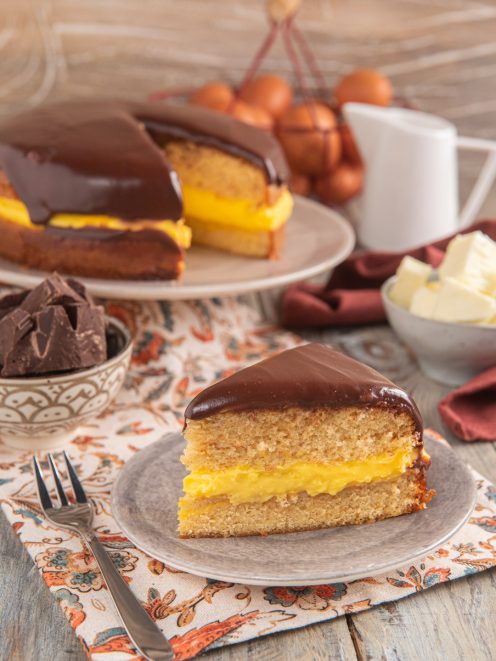 Fetta di Boston cream pie con crema pasticcera gialla tra due strati soffici e glassa al cioccolato