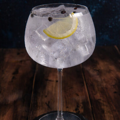 Gin tonic con ghiaccio abbondante, fetta di limone e bacche di ginepro